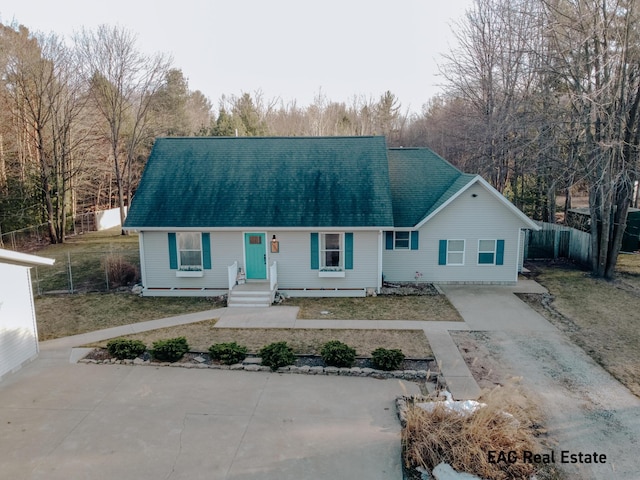 view of front facade featuring driveway, roof with shingles, and fence