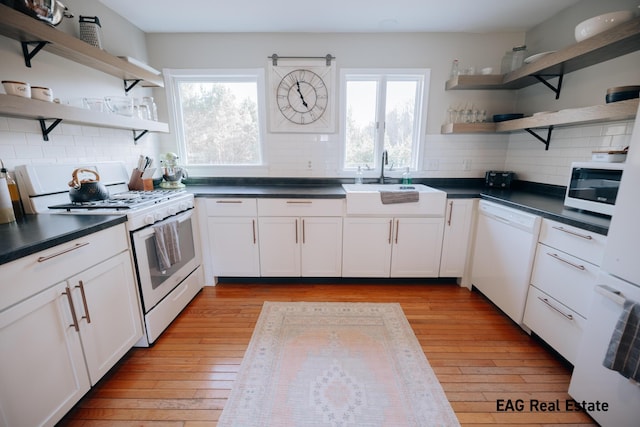 kitchen with light wood-type flooring, open shelves, a sink, dark countertops, and white appliances