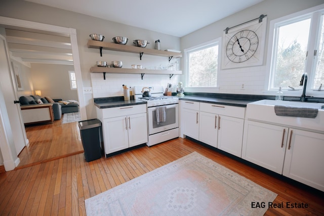 kitchen with light wood finished floors, dark countertops, backsplash, white gas stove, and a sink