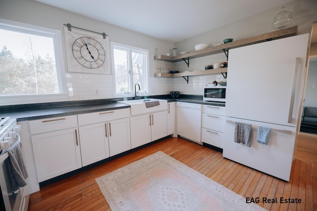 kitchen featuring dark countertops, backsplash, white dishwasher, stove, and a sink