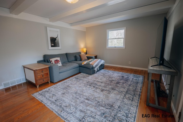 living area featuring visible vents, baseboards, beamed ceiling, and wood finished floors