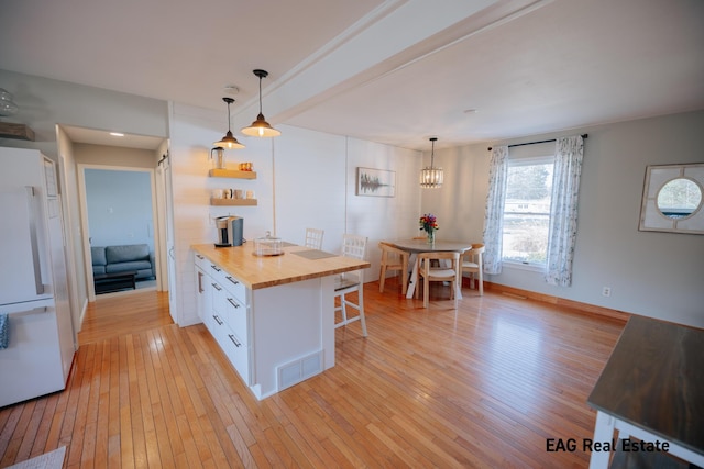 kitchen featuring light wood-style flooring, butcher block counters, a kitchen bar, and white fridge