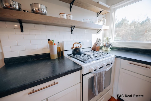 kitchen with white gas stove, tasteful backsplash, dark countertops, and open shelves