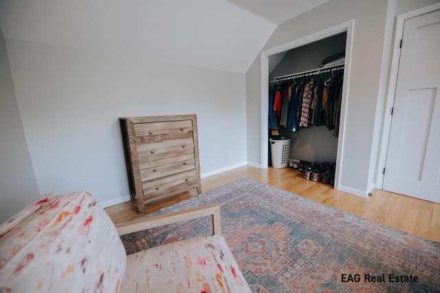 bedroom with a closet, wood finished floors, baseboards, and vaulted ceiling