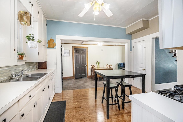 kitchen with crown molding, white cabinets, light wood finished floors, and a sink