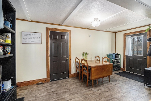 dining room featuring baseboards, a textured ceiling, wood finished floors, and crown molding