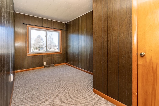 spare room featuring carpet flooring, baseboards, visible vents, and wood walls