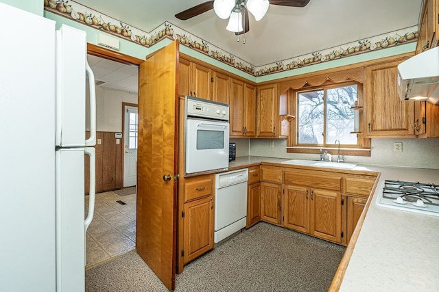 kitchen featuring light floors, light countertops, brown cabinetry, white appliances, and a sink