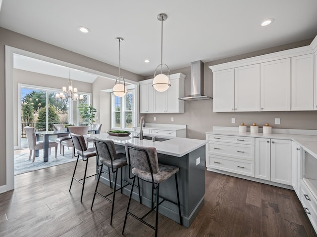 kitchen featuring wall chimney range hood, a sink, a center island with sink, a kitchen bar, and white cabinetry