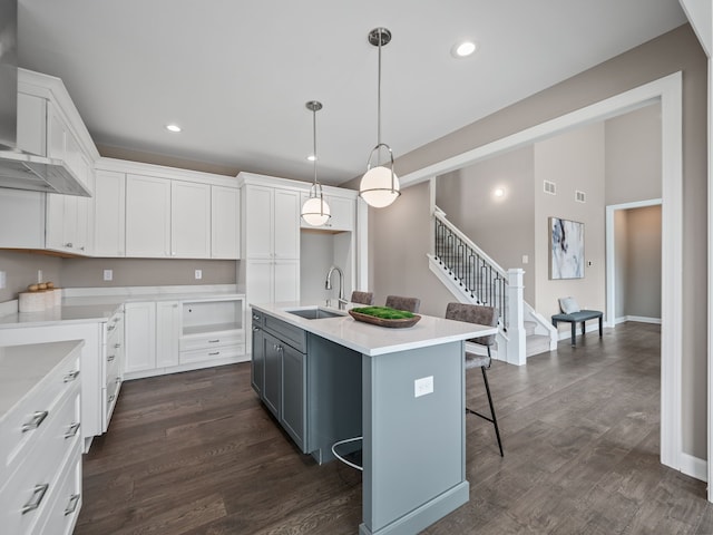 kitchen featuring dark wood-type flooring, a sink, white cabinetry, and wall chimney range hood