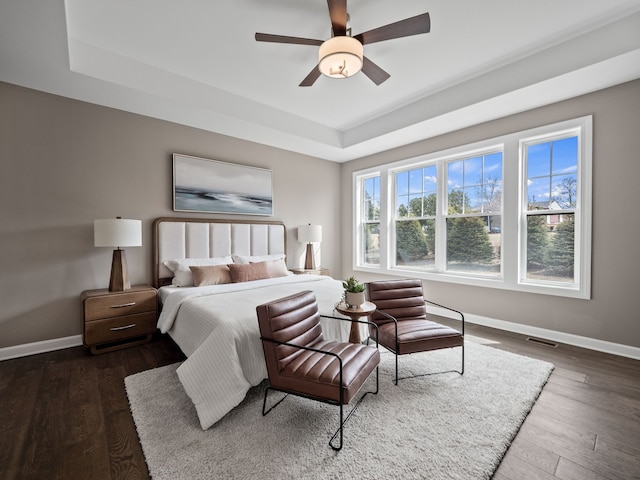 bedroom with baseboards, wood finished floors, a tray ceiling, and a ceiling fan