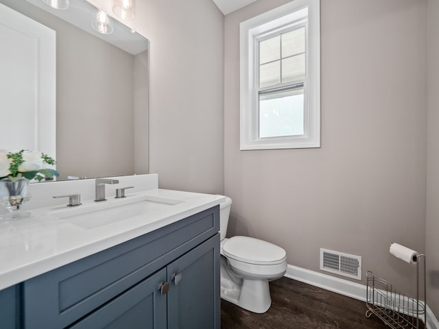 bathroom featuring toilet, baseboards, visible vents, wood finished floors, and vanity