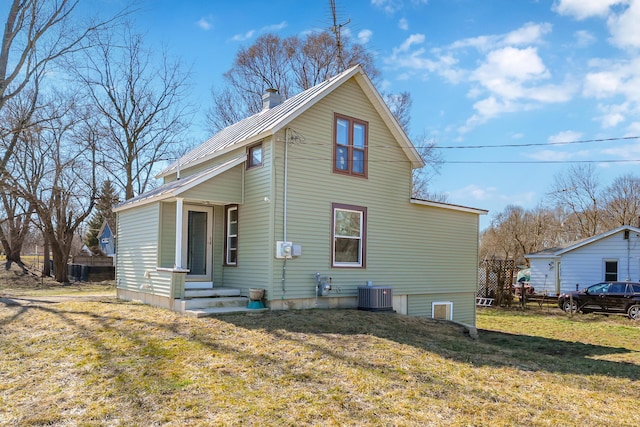 back of property with a lawn, cooling unit, a chimney, and metal roof