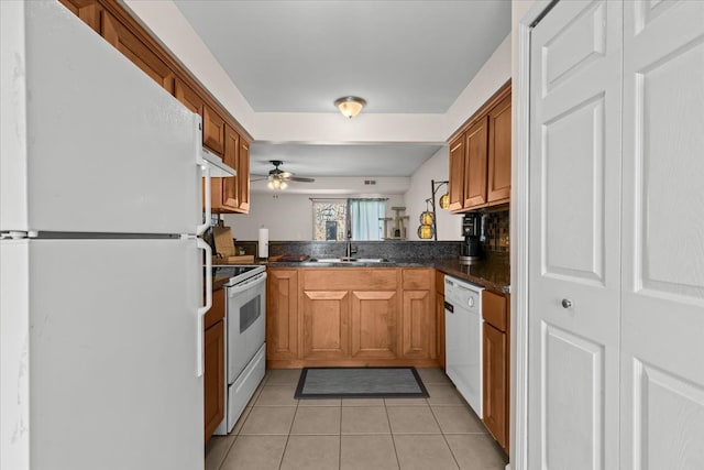 kitchen featuring light tile patterned floors, white appliances, dark countertops, and brown cabinetry