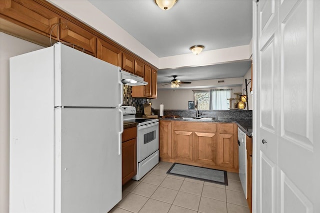 kitchen featuring white appliances, brown cabinetry, dark countertops, and under cabinet range hood