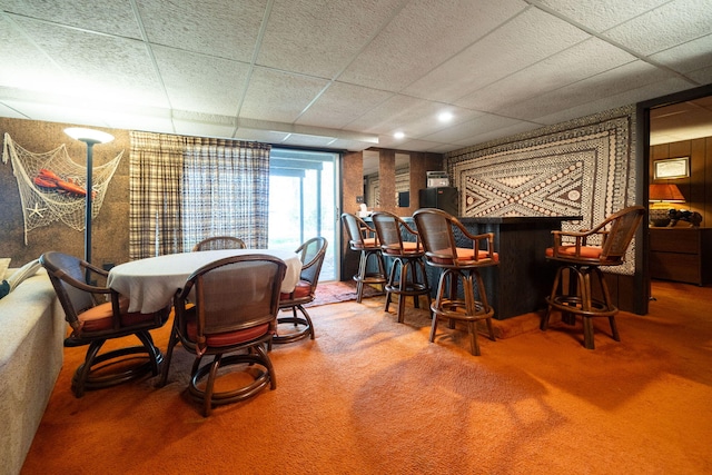 carpeted dining space with a bar and a paneled ceiling