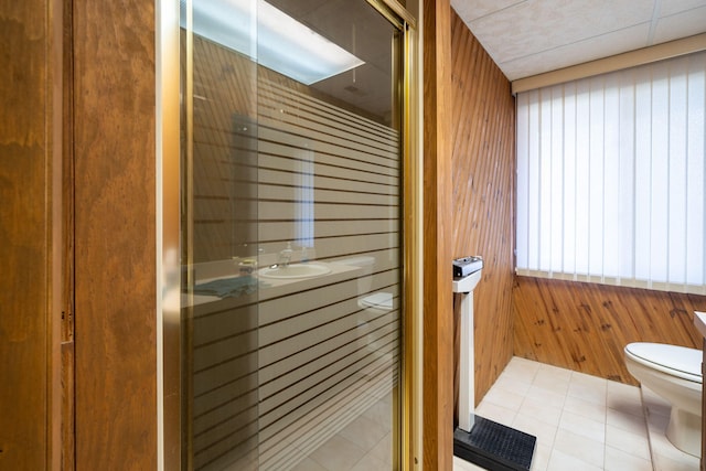 bathroom featuring tile patterned flooring, a shower stall, toilet, and wood walls