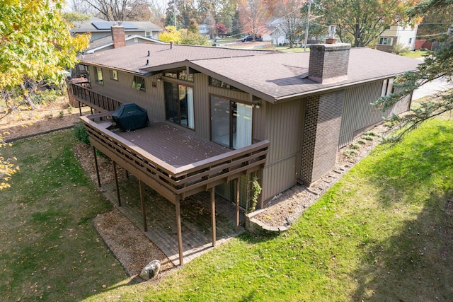 back of property with a wooden deck, a lawn, roof with shingles, and a chimney