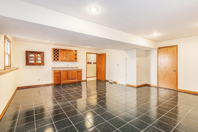 unfurnished living room featuring baseboards, a sink, indoor wet bar, a textured ceiling, and dark tile patterned floors