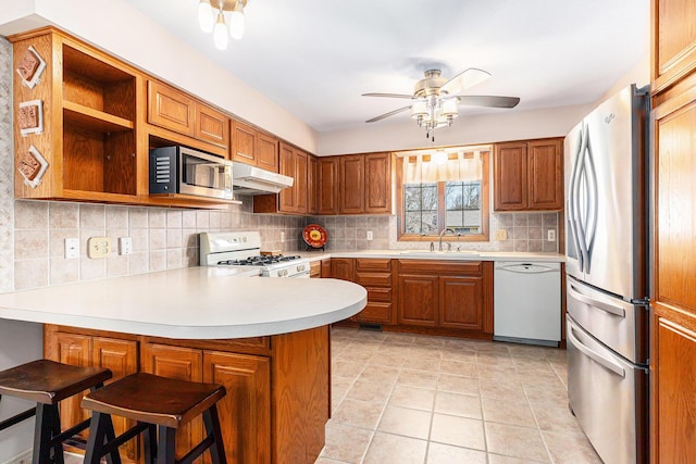 kitchen with backsplash, under cabinet range hood, a peninsula, stainless steel appliances, and a sink