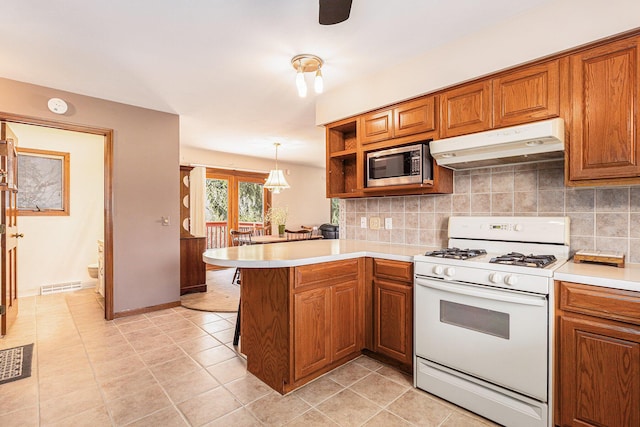 kitchen featuring under cabinet range hood, stainless steel microwave, white gas stove, and brown cabinetry