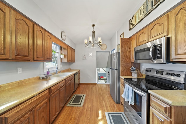 kitchen featuring light countertops, brown cabinets, appliances with stainless steel finishes, light wood-style floors, and a sink