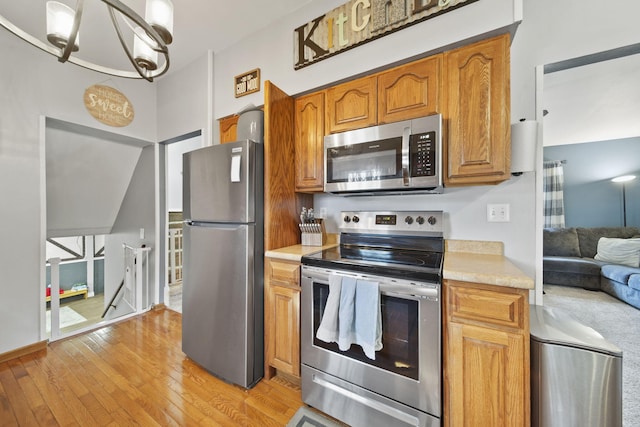 kitchen featuring light countertops, light wood-style flooring, appliances with stainless steel finishes, an inviting chandelier, and brown cabinetry