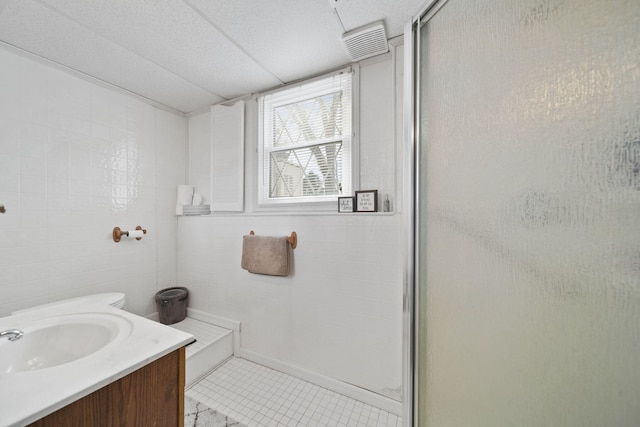 full bath with tile patterned flooring, visible vents, tile walls, a stall shower, and vanity