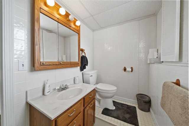 bathroom with tile patterned flooring, a drop ceiling, toilet, vanity, and tile walls