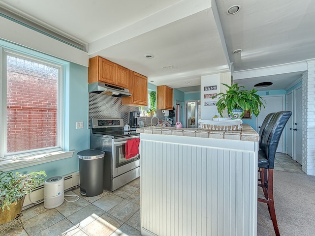 kitchen with brown cabinetry, stainless steel electric range, tile counters, under cabinet range hood, and backsplash