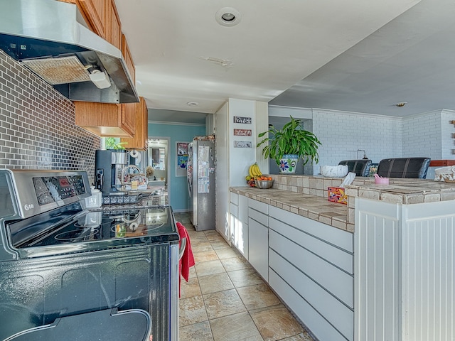 kitchen with tile counters, under cabinet range hood, open floor plan, appliances with stainless steel finishes, and a peninsula