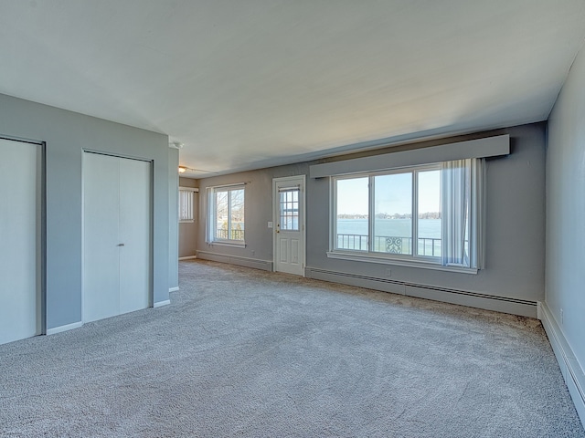 unfurnished bedroom featuring carpet floors, baseboard heating, and multiple closets