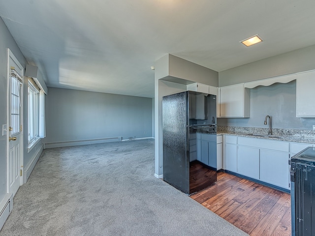 kitchen with light stone counters, freestanding refrigerator, a sink, white cabinets, and electric stove