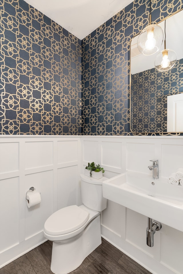 bathroom with a wainscoted wall, wallpapered walls, toilet, and wood finished floors