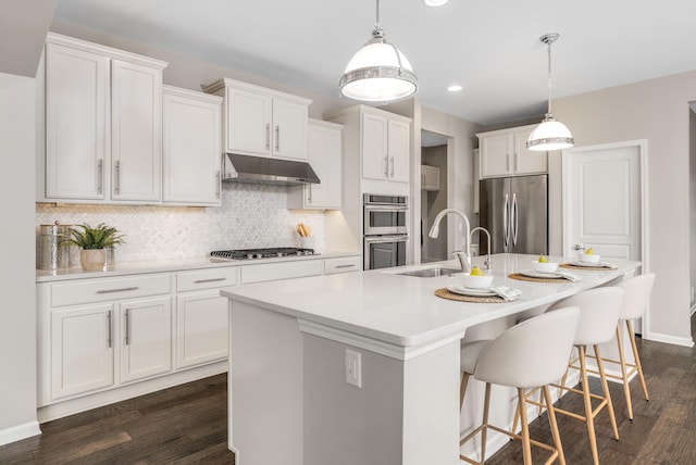 kitchen with under cabinet range hood, backsplash, dark wood finished floors, white cabinetry, and stainless steel appliances