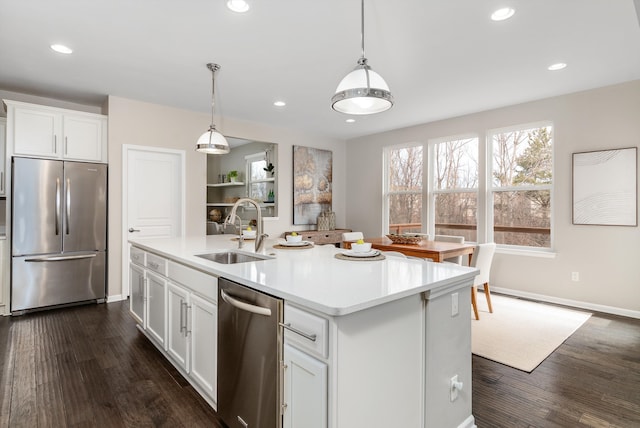 kitchen with dark wood-type flooring, an island with sink, a sink, stainless steel appliances, and light countertops