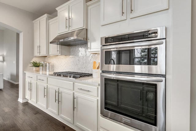 kitchen with under cabinet range hood, backsplash, dark wood finished floors, appliances with stainless steel finishes, and light countertops