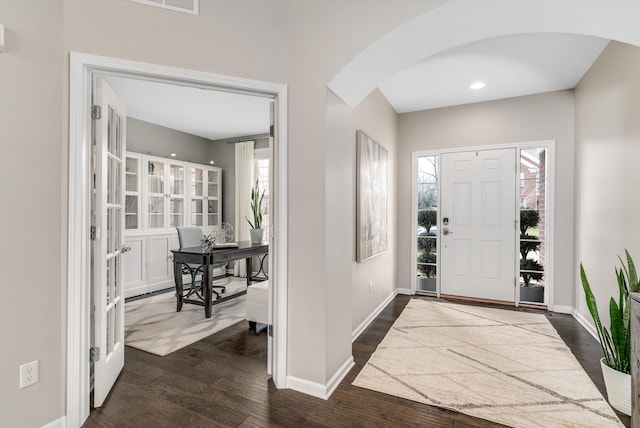 foyer featuring arched walkways, dark wood-type flooring, and baseboards