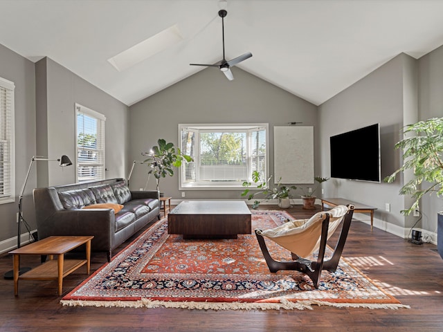 living area featuring a ceiling fan, vaulted ceiling with skylight, wood finished floors, and baseboards