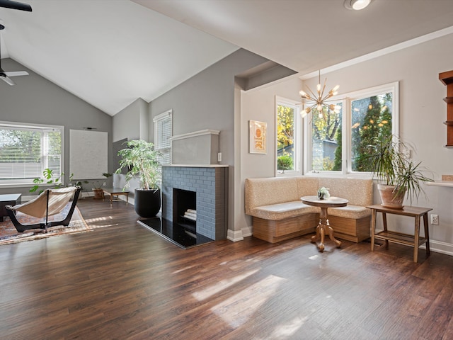 living area featuring a brick fireplace, baseboards, lofted ceiling, ceiling fan with notable chandelier, and wood finished floors