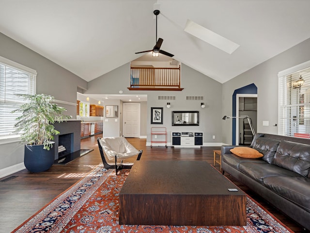 living room featuring a ceiling fan, wood finished floors, visible vents, high vaulted ceiling, and a skylight