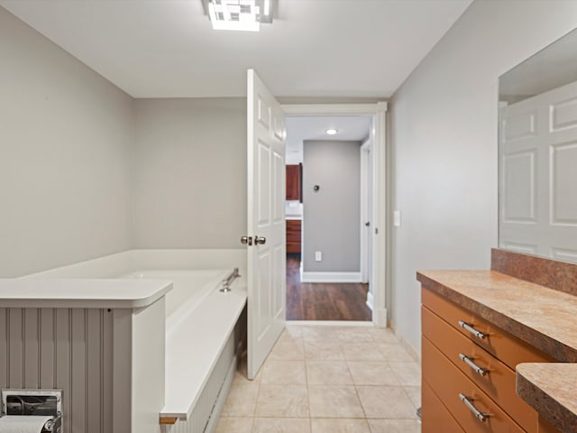 full bathroom with tile patterned flooring, a garden tub, vanity, and baseboards