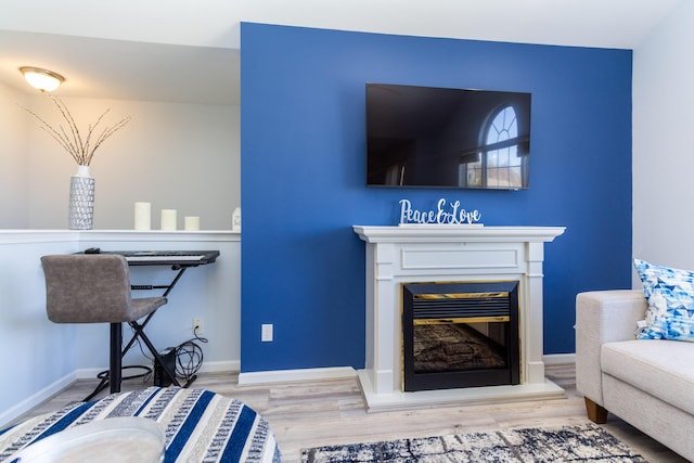 living area with a glass covered fireplace, baseboards, and wood finished floors