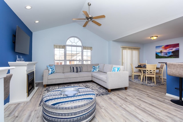 living room with a glass covered fireplace, lofted ceiling, baseboards, and light wood-type flooring