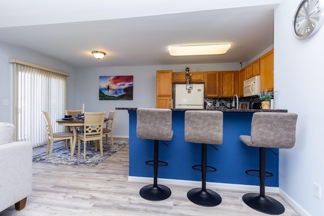 kitchen featuring a breakfast bar, white appliances, a peninsula, and light wood finished floors