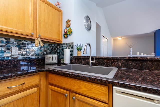 kitchen with decorative backsplash, dark stone counters, white dishwasher, and a sink