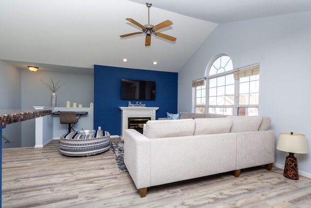 living room with wood finished floors, a glass covered fireplace, recessed lighting, baseboards, and vaulted ceiling