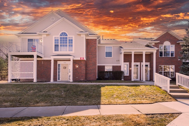 view of front facade featuring brick siding, a balcony, and a front yard