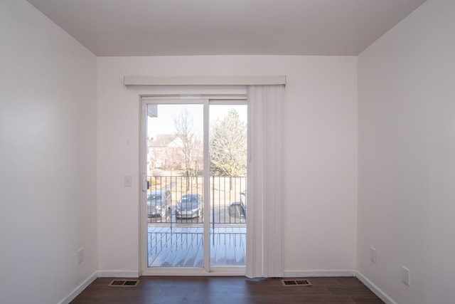 empty room featuring visible vents, dark wood-type flooring, and baseboards