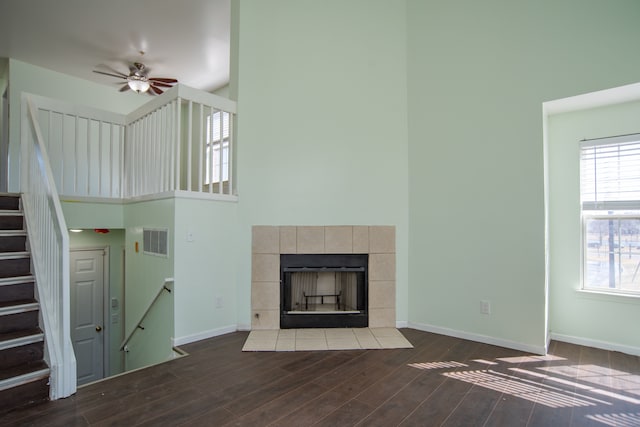 unfurnished living room featuring dark wood-style floors, baseboards, visible vents, a high ceiling, and a tile fireplace